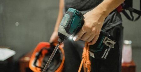 Mesin Bor Impact Cordless - A worker holding a power drill and helmet, ready for maintenance tasks.