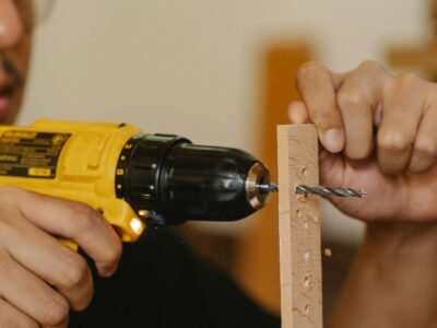 Mesin Bor Impact Cordless - A craftsman using a yellow drill to create holes in a wooden plank indoors.