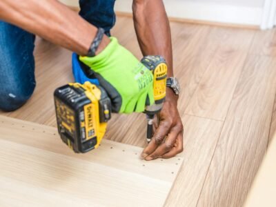 Mesin Bor Impact Cordless - Close-up of handyman drilling wood indoors with green gloves and cordless drill.