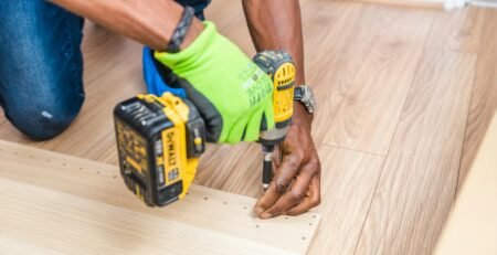 Mesin Bor Impact Cordless - Close-up of handyman drilling wood indoors with green gloves and cordless drill.